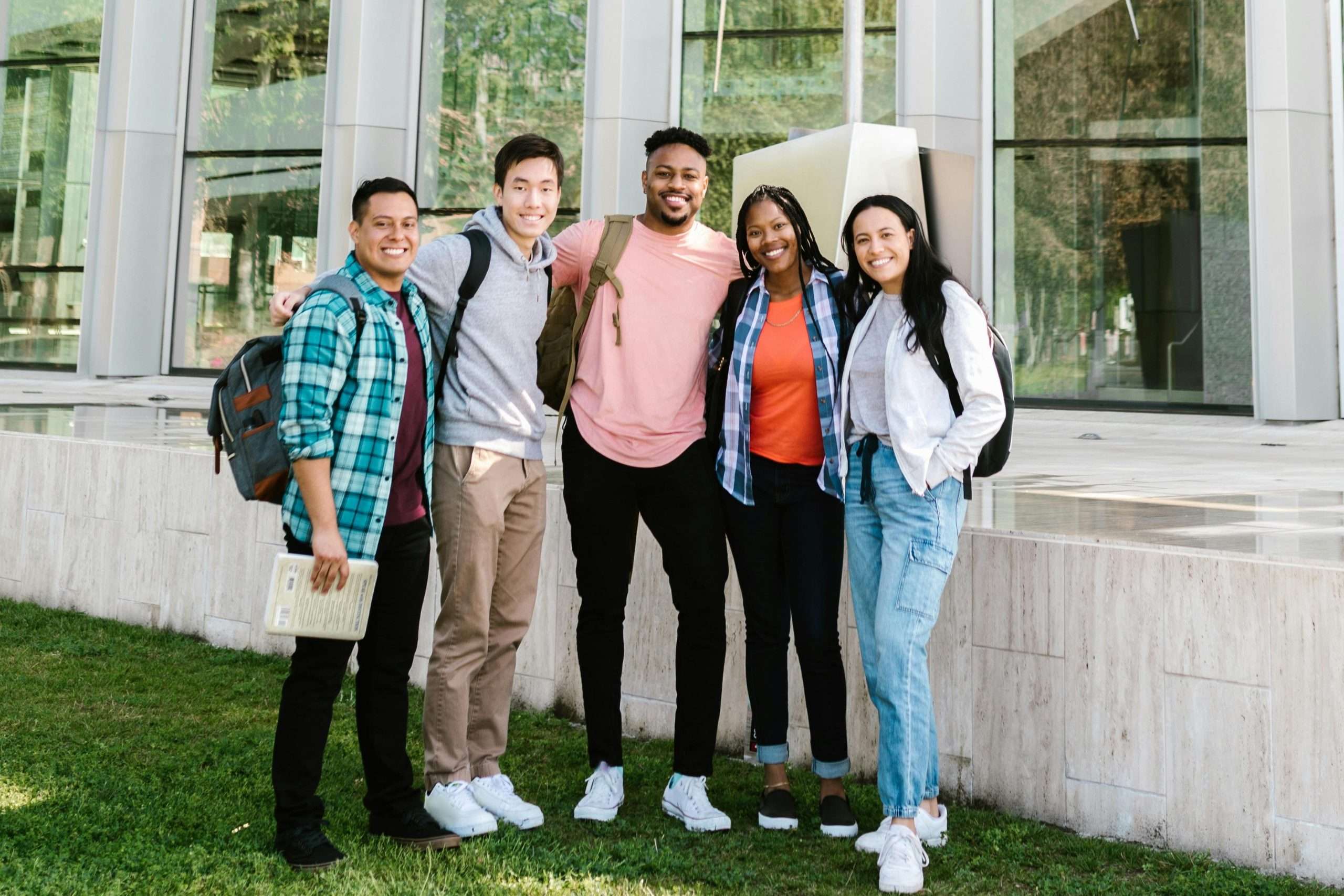 Cheerful group of diverse students standing outside a modern educational building on a sunny day.