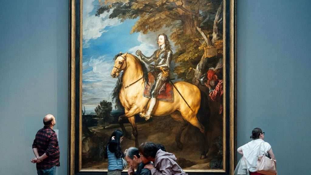 Art enthusiasts admiring a large historical painting in The Clore Room, museum setting in England.