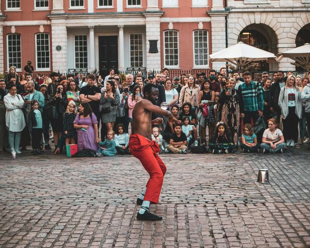 A street performer entertains a diverse crowd in Covent Garden, London, showcasing vibrant street culture.